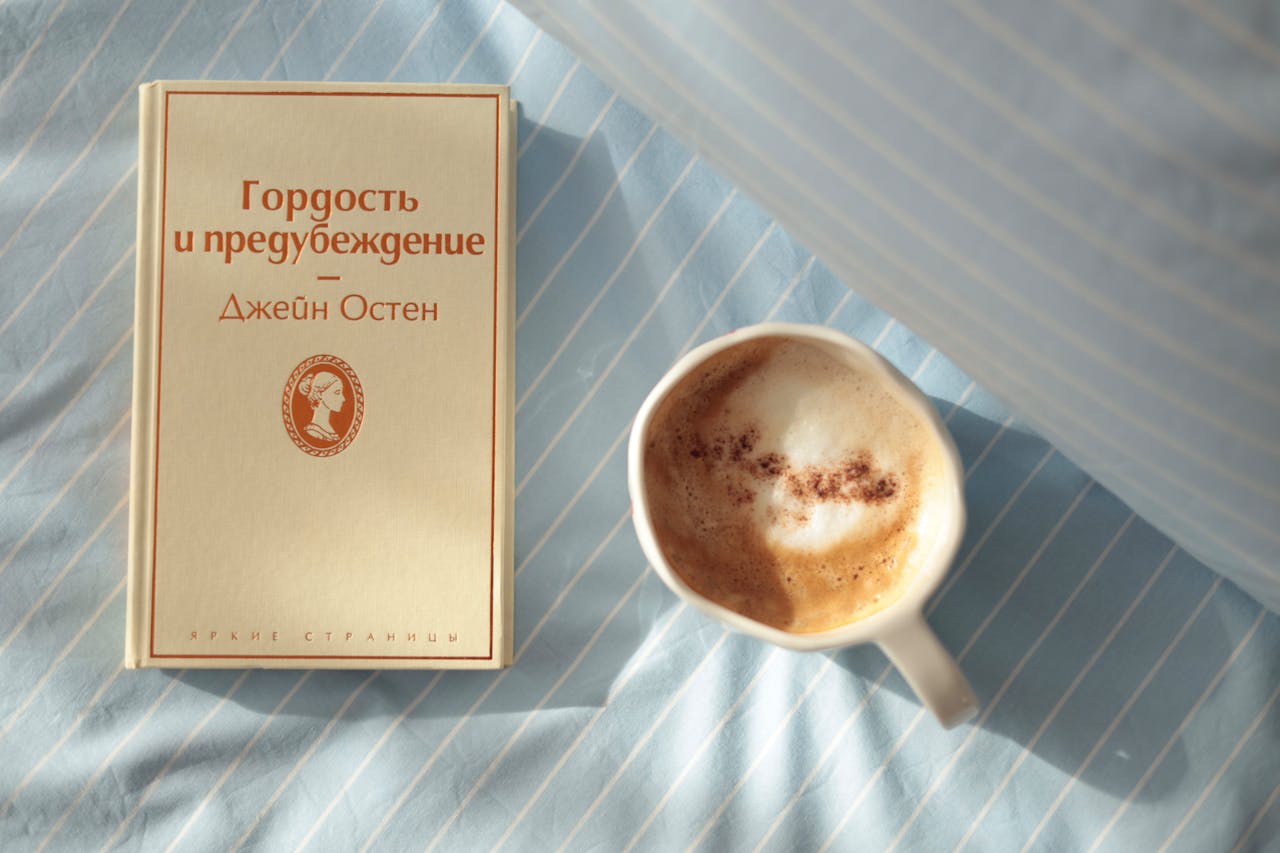 A calm morning scene with a cup of coffee and a book on a striped bedsheet.